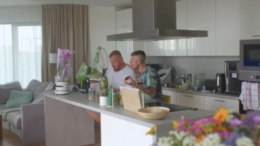İki adam apartman dairesinde kahvaltı yapıyor. Masaya otururlar, yemek yerler..