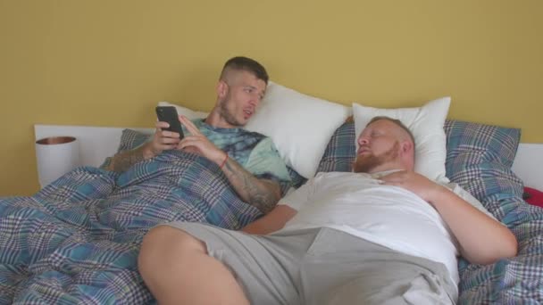 ゲイデートアプリ。二人の髭の男が電話でベッドに横になってキスをして. — ストック動画