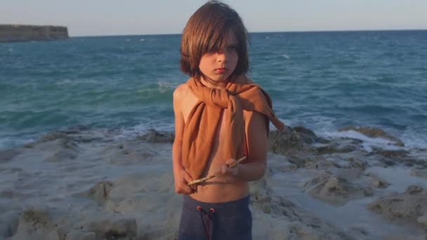 Porträtt av ett barn vid havet. Han håller ett spjut i sina händer. Överlevnad spel. — Stockvideo