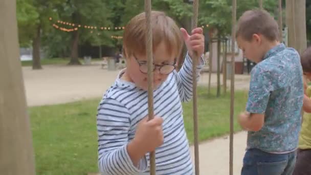 El niño del síndrome de Down se abre paso sobre una cuerda de obstáculos, se toma de la mano, mueve la corte. — Vídeos de Stock