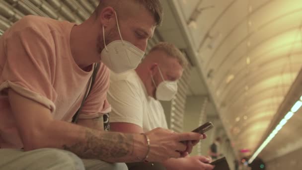 Мужчины в масках используют мобильное приложение на вокзале — стоковое видео