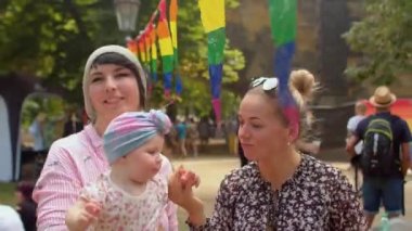 Çocuklu mutlu LGBT çifti gökkuşağı bayraklarının yanında yürüyor. Bebekli aile.