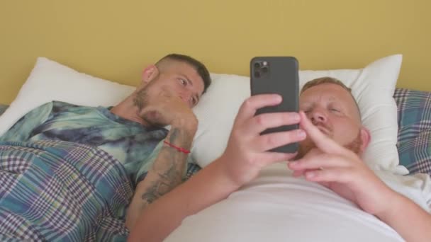 God morgen på soverommet. Lykkelig ung mann med elskeren sin bruker telefon. – stockvideo