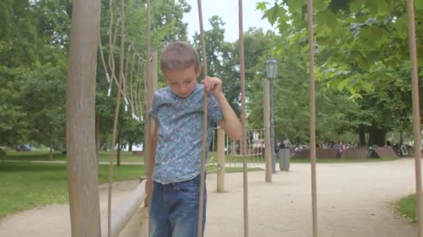 Adolescente en jeans sube sobre cuerdas patio de recreo. Balanzas con cuerdas. — Vídeos de Stock
