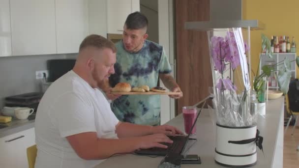 Junge schwule Mann bietet seine Geliebte mit Laptop-Brötchen zum Frühstück. Richtige Ernährung — Stockvideo