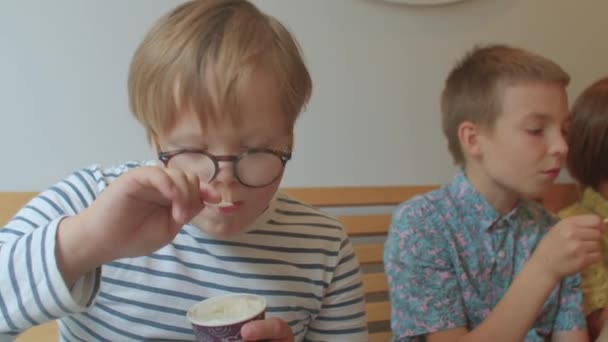 Junge mit Down-Syndrom isst im Café Eis mit Löffel. Fokus auf Lebensmittel, Gläser an. — Stockvideo