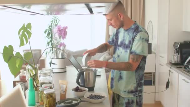 Человек готовит коктейли на завтрак. Он ломает сливы ставит их блендер на кухне. — стоковое видео