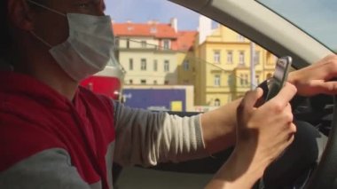 Maskeli sürücü araba kullanıyor. Telefon kullanıyor. Mobil uygulama kullanılıyor
