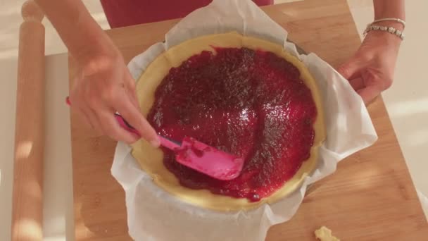 A pink spatula spreads red jam on a dough base before baking. Jam tart in Italy. — Stock Video