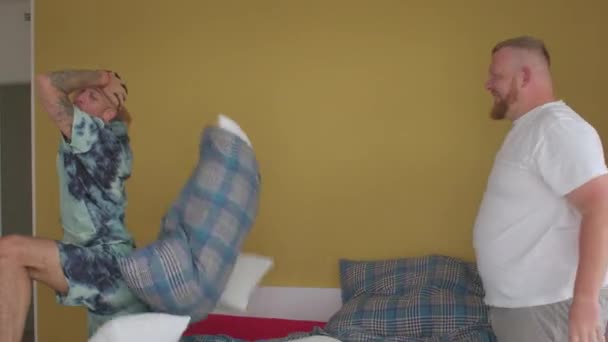 Παιχνιδιάρικη διάθεση σε ένα ζευγάρι. Δύο τύποι αρχίζουν να πηδάνε μαξιλάρια στο κρεβάτι στην κρεβατοκάμαρα.. — Αρχείο Βίντεο
