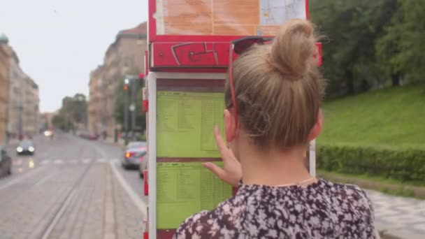 Mladá žena se dívá na jízdní řád novin tramvají na zastávce městské hromadné dopravy. — Stock video