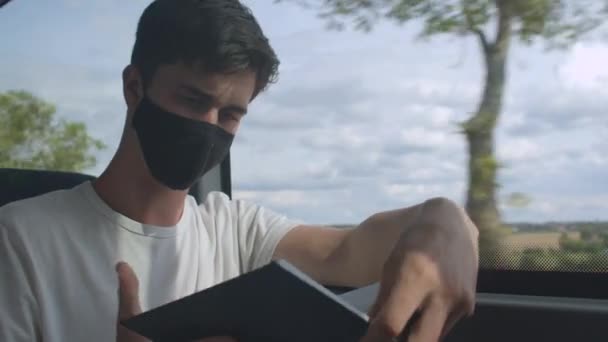 Een slimme man met een masker leest een boek over openbaar vervoer in beweging. Focus op pagina 's. — Stockvideo