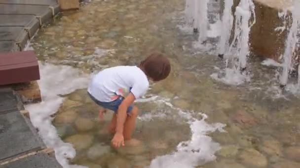 Dziecko spaceruje w wodzie miejskiej fontanny w upalny dzień w parku. — Wideo stockowe