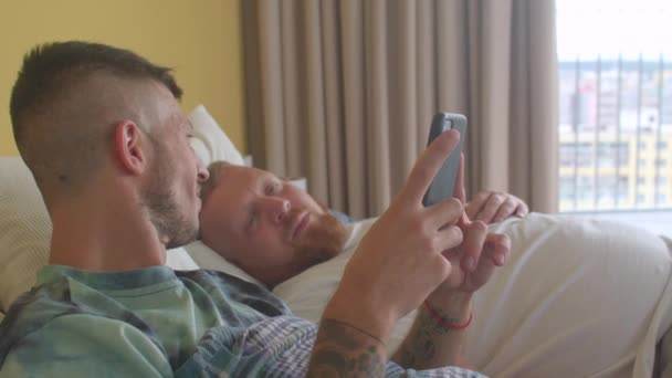 Dimineaţa în dormitor. Un tânăr homosexual fericit cu iubitul său folosește telefonul. — Videoclip de stoc