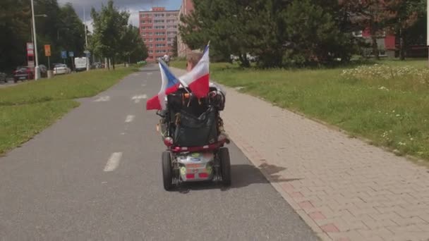 Pessoa com deficiência se move pela cidade em cadeira de rodas com bandeiras checas. — Vídeo de Stock