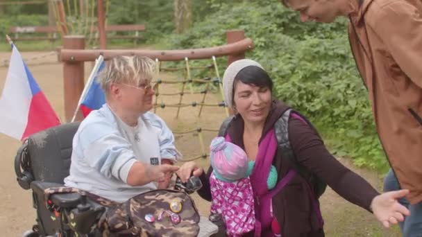 Член семьи с инвалидностью в инвалидной коляске встречается с родственниками. На открытом воздухе. — стоковое видео