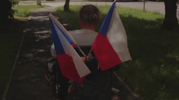 Человек с ограниченными возможностями передвигается в инвалидной коляске с чешскими флагами. Закрыть. — стоковое видео