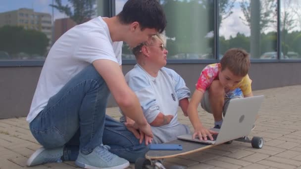 Handikappad person med en skateboard omgiven av vänner med hjälp av bärbar dator. — Stockvideo