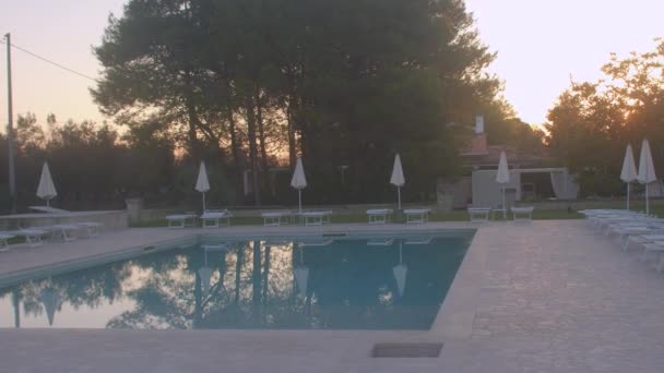 Pool in the evening. The umbrellas are folded sun peeping out from behind tree — Stock Video