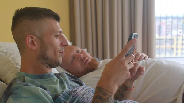 Manhã no quarto. feliz jovem gay homem com seu amante usa telefone. — Fotografia de Stock