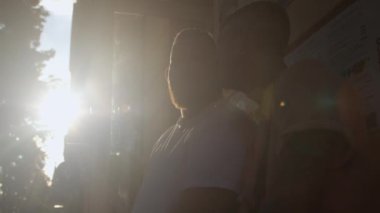 Şehirde erkekler gün ışığında konuşurlar. Bardaktan bir yudum alır.