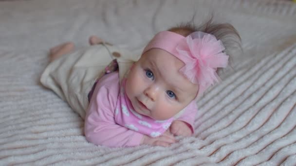 Porträt eines kleinen Mädchens mit einer rosa Schleife auf dem Kopf, das auf dem Bett liegt — Stockvideo