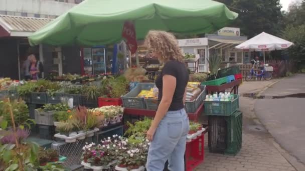 Mulher escolhe comprar mercado de flores. Ela olha para as plantas e faz uma escolha — Vídeo de Stock