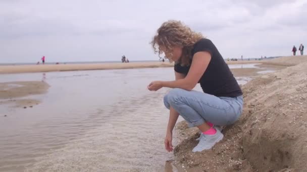 Dívka hodí kamínky do vody. Sedí u řeky, ponořená v myšlenkách. — Stock video