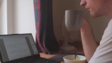 Çocuklar bir bardak sıcak içecek kaldırıyor. Masaya oturur, dizüstü bilgisayar kullanır..