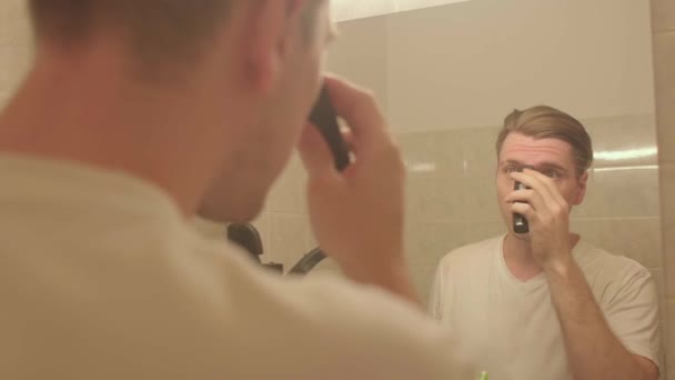 Ein Mann schneidet sich mit einem Haarschneider die Augenbrauen ab. Er bereitet den Look für das Date vor. — Stockvideo