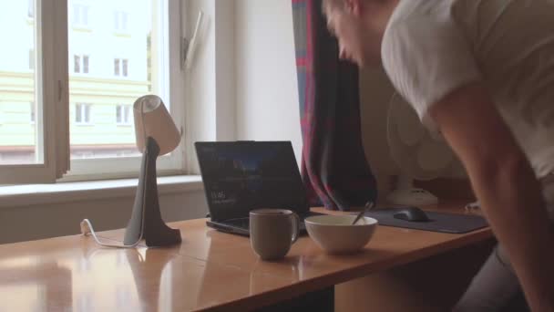 Killen sätter sig vid bordet med en laptop i början av dagen. — Stockvideo