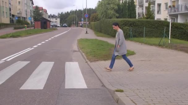 Женщина переходит дорогу с помощью пешеходного перехода, отмечая белые полосы на дороге — стоковое видео