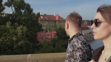 Adam ve kadın şehirde cadde boyunca ilerliyorlar. Gözlerinin üstüne siyah gözlük takıyor.