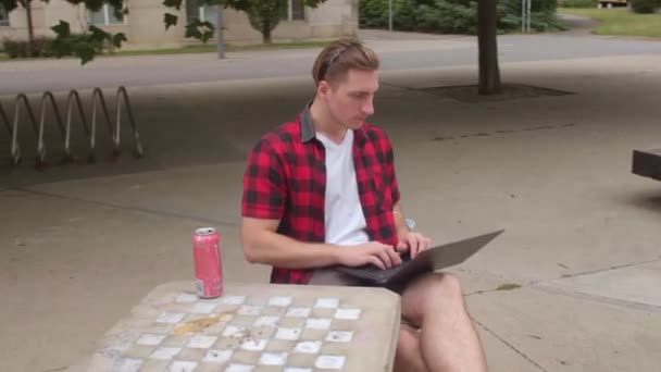 Mladý muž používá laptop v městském parku. Šachovnice. Běžná práce v počítači — Stock video