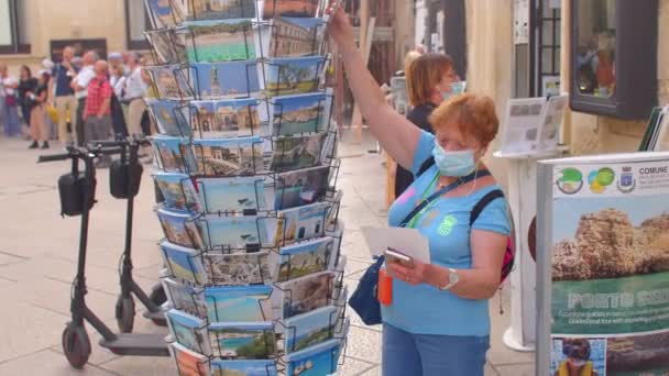 La mujer enmascarada elige una postal para comprar. Impacto de los bloqueos en los negocios de viajes — Vídeos de Stock