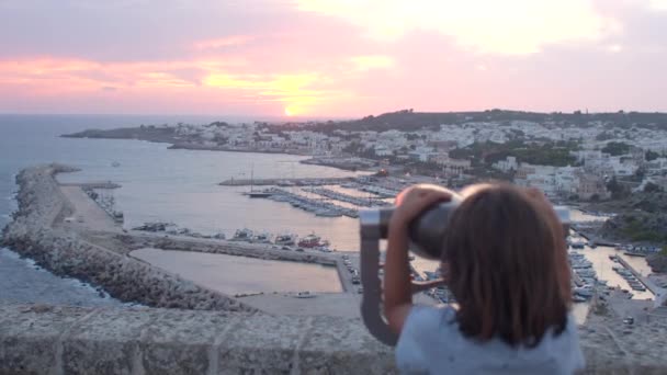 Child looks at the buildings coastal town with the binocular vending machine. — Stockvideo