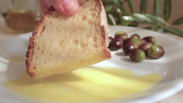 Χέρι με ψωμί βυθίζει την άκρη σε εξαιρετικό παρθένο ελαιόλαδο, ελιές είναι σε ένα πιάτο. — Αρχείο Βίντεο