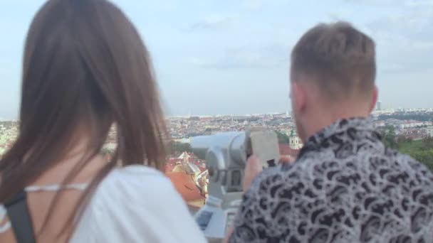 El tipo y la chica de espaldas en el panorama de la ciudad. Están cerca del dispositivo de visión. — Vídeos de Stock