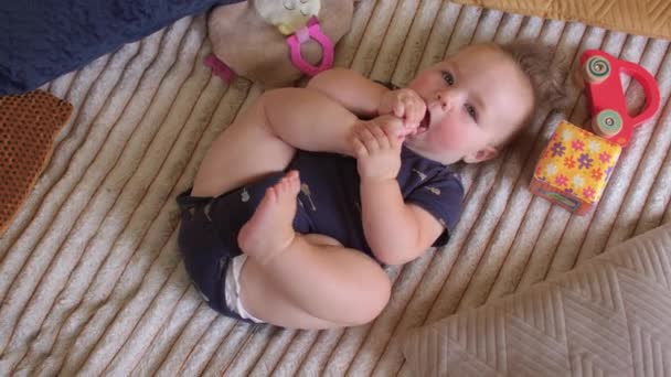 Bayi berusia enam bulan menaruh kaki di mulutnya. Otot yang baik flex flail anggota badan. — Stok Video