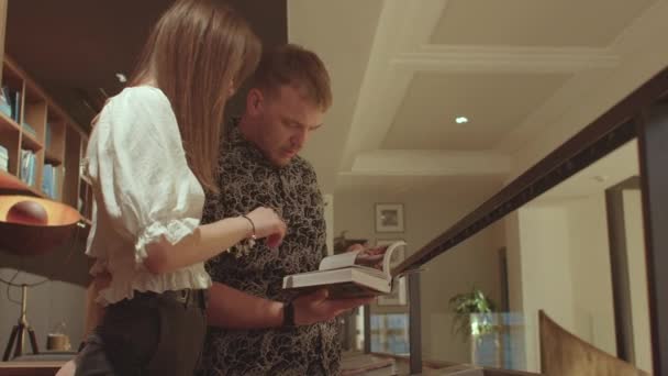 Meisje en jongen lezen een boek in de bibliotheek. Hij bladert door de pagina 's.. — Stockvideo