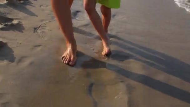 母と子の裸の足は海のビーチのぬれた砂に沿って移動します。. — ストック動画