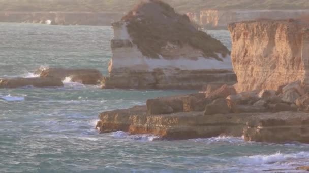 Fale wody morskiej zderzają się ze skałami wybrzeża. Światło oświetla skałę — Wideo stockowe
