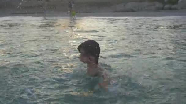 Radostné dítě se koupe ve vodě z moře. Vrhá se po hlavě. Užijte si vodu. — Stock video