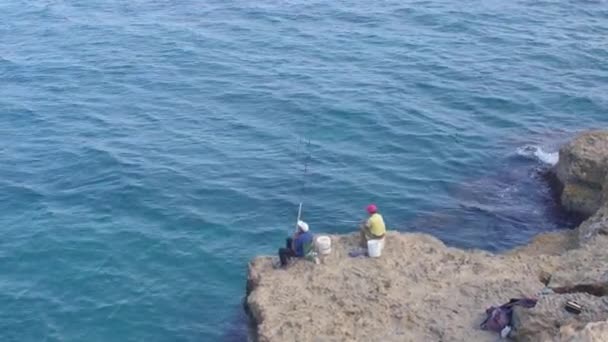 Dos pescadores en la orilla del mar están pescando. El hombre saca una caña de pescar. — Vídeos de Stock