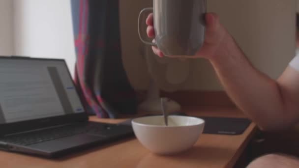 Man takes mug drink with hands. Against background laptop — стоковое видео