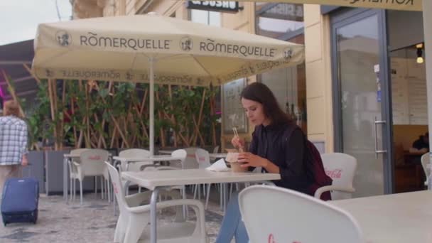 Girl eats street food at table in cafe umbrella protects from rain and sun — стоковое видео