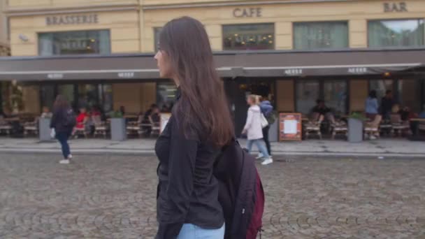 Camera rotation girl stands street city. She carries a backpack shoulder — стокове відео