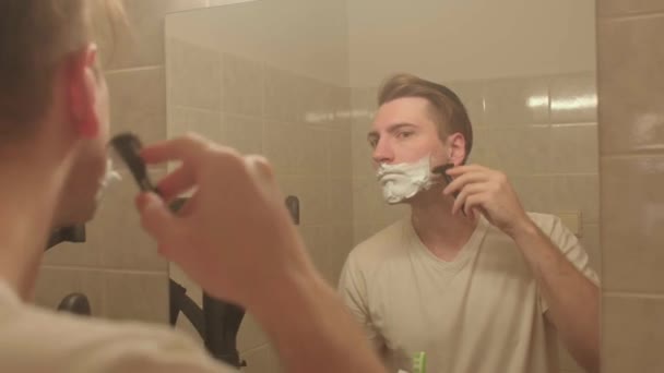 El hombre se afeita la cara mojada. Usa una navaja para cortarle los pelos de la cara.. — Vídeo de stock