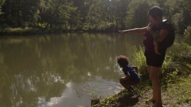 Anne ve yeni doğmuş bir bebek taşıyıcısı ile çocuk şehir göletinde suyla oynuyor.