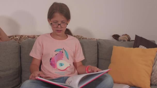 Ένα κορίτσι με γυαλιά κρατάει ένα βιβλίο στα χέρια της. Γυρίζει τις σελίδες. — Αρχείο Βίντεο
